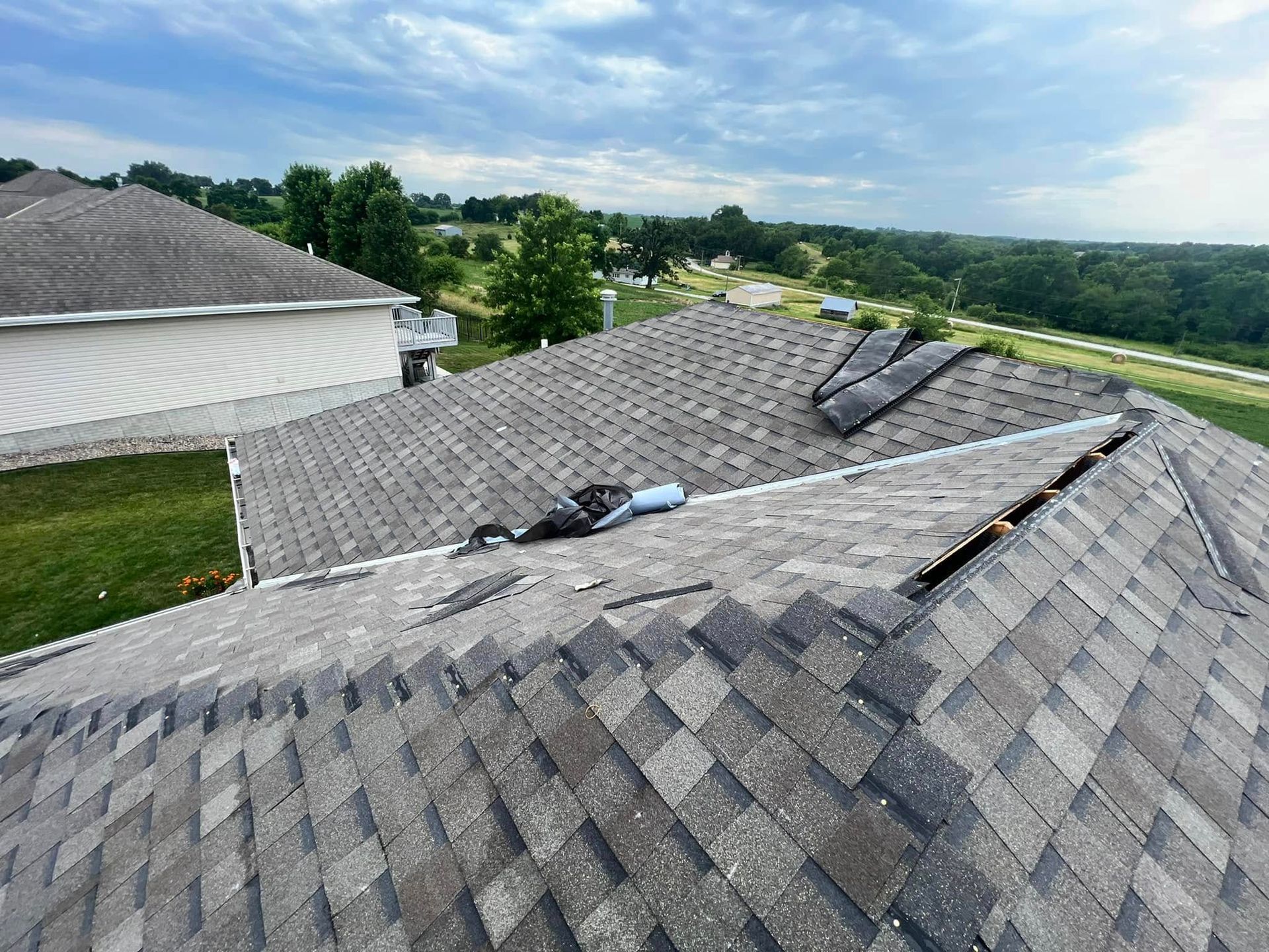 Damaged shingled roof with missing sections and exposed underlayment, viewed from above in a suburban area