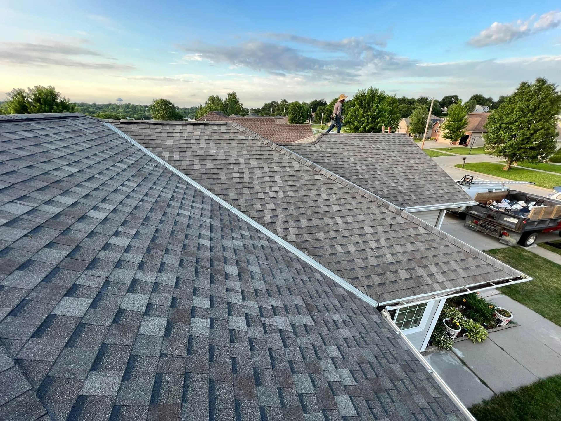 Roofing shingles on a large house under construction, with workers and trees in the background