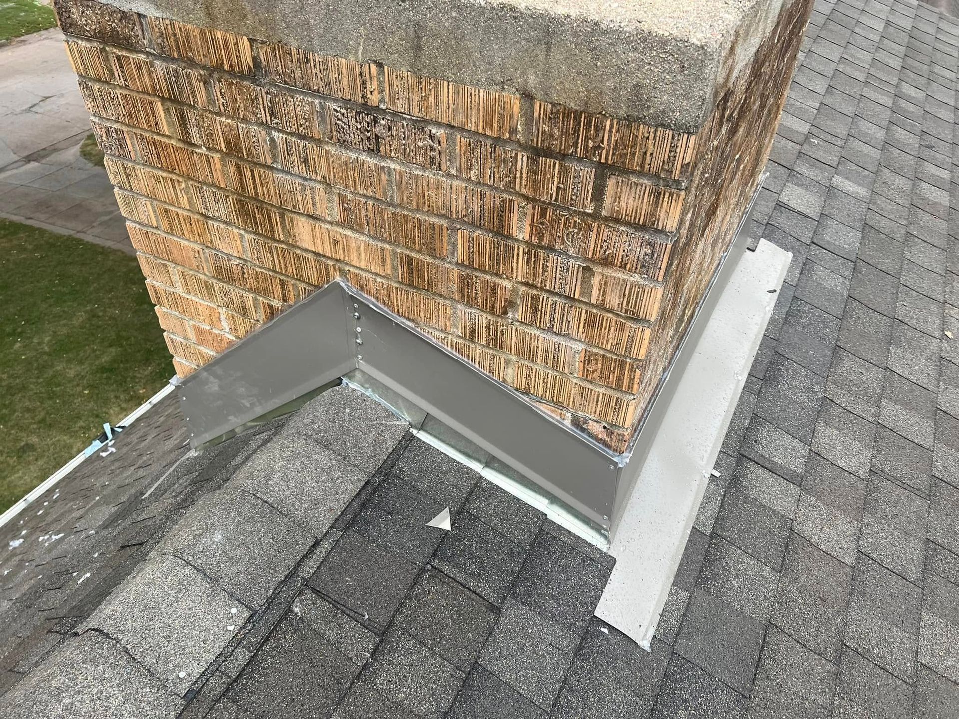 Brick chimney with gray metal flashing on a shingled roof corner