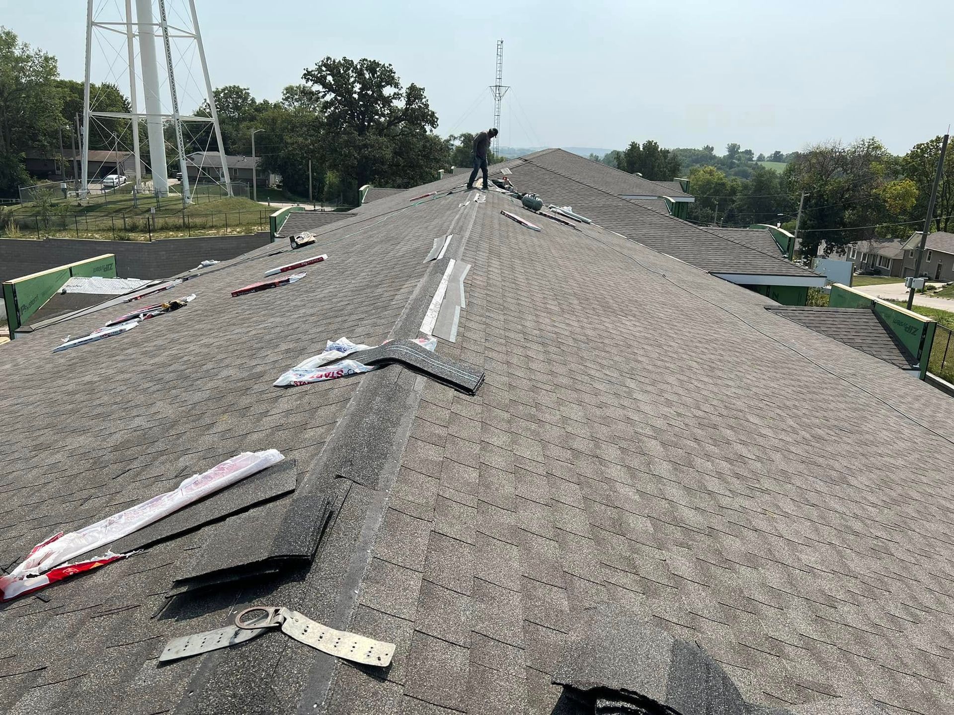 Damaged shingle roof with scattered debris and a worker near the ridge line
