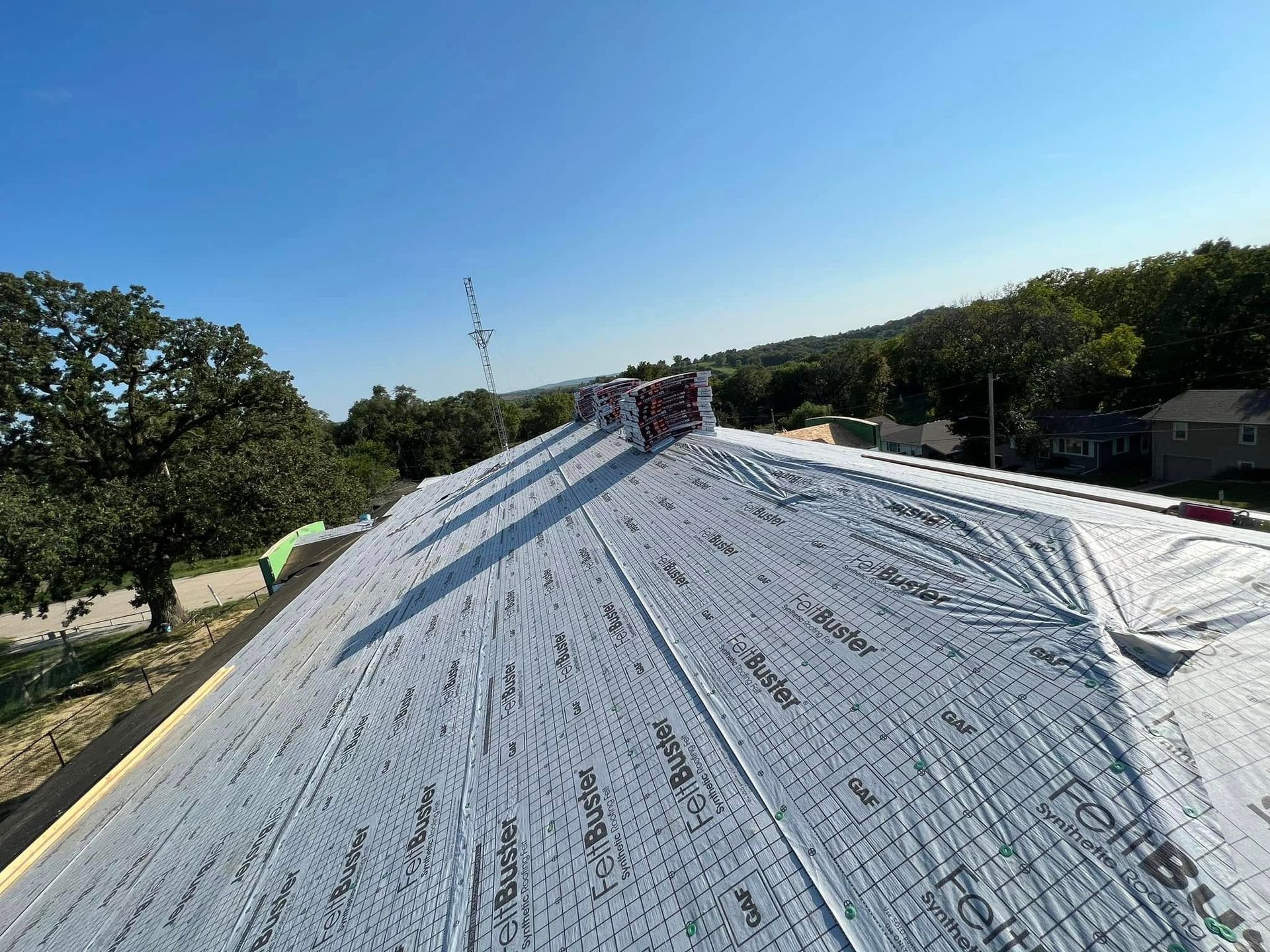 Workers on a steep white roof under a clear blue sky, with trees and fields in the background.