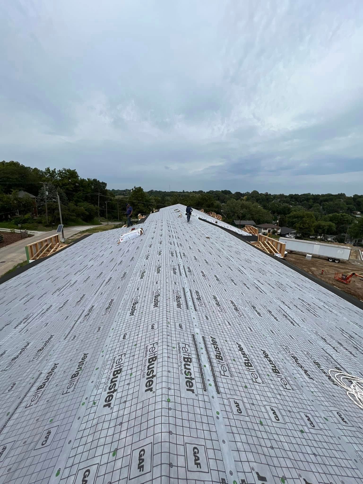 Person standing on a white rooftop under a cloudy sky, overlooking green trees and a distant town