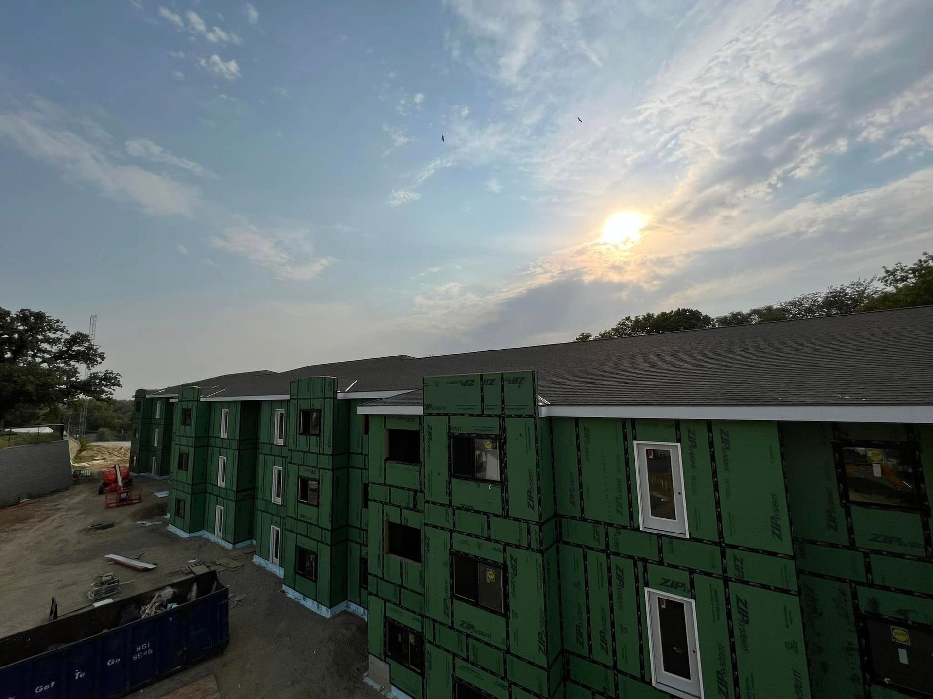 Green modular buildings under construction at sunset, with a bright sky overhead.