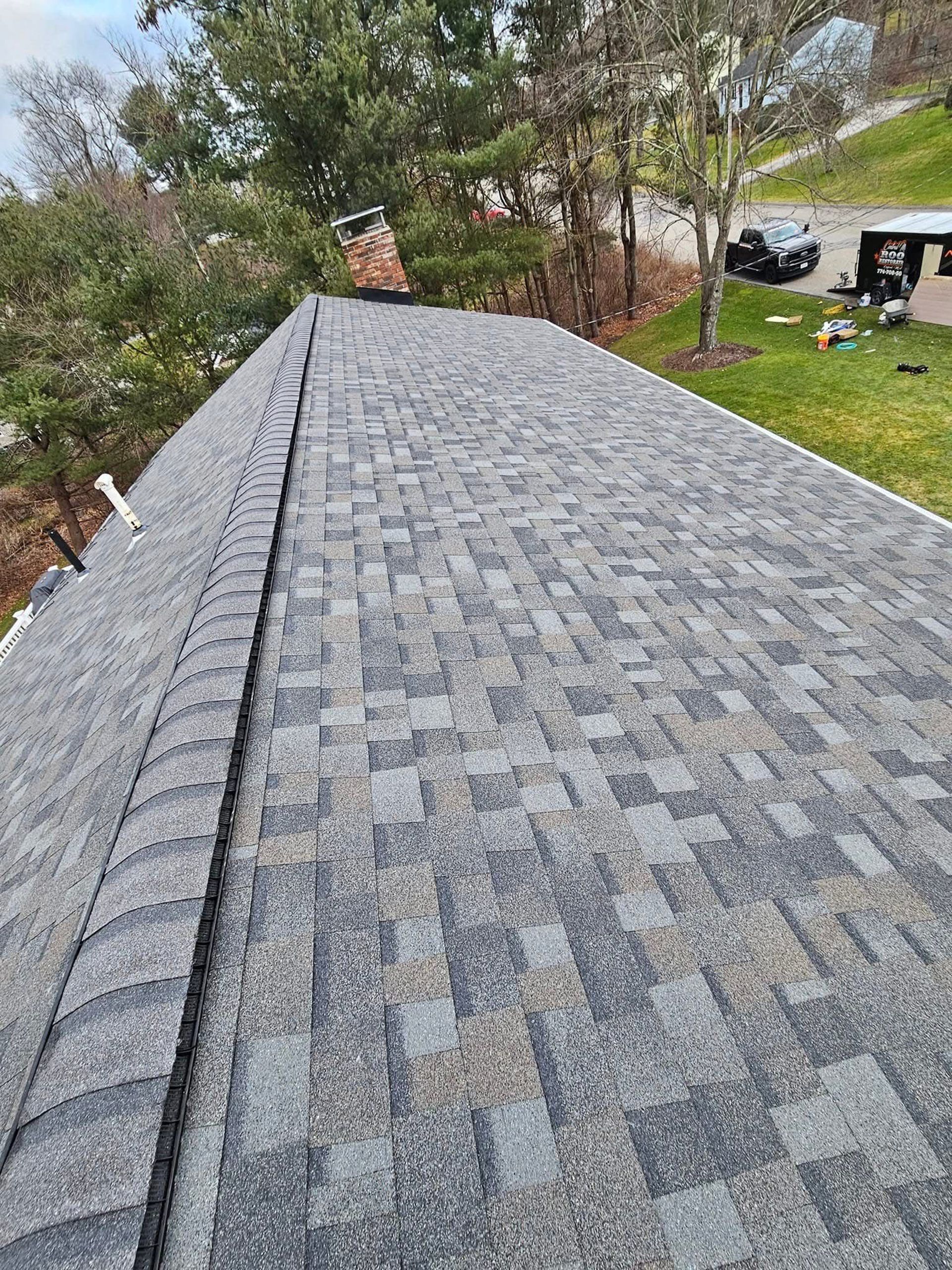 Gray shingled roof viewed from above, with trees and a grassy yard in the background.