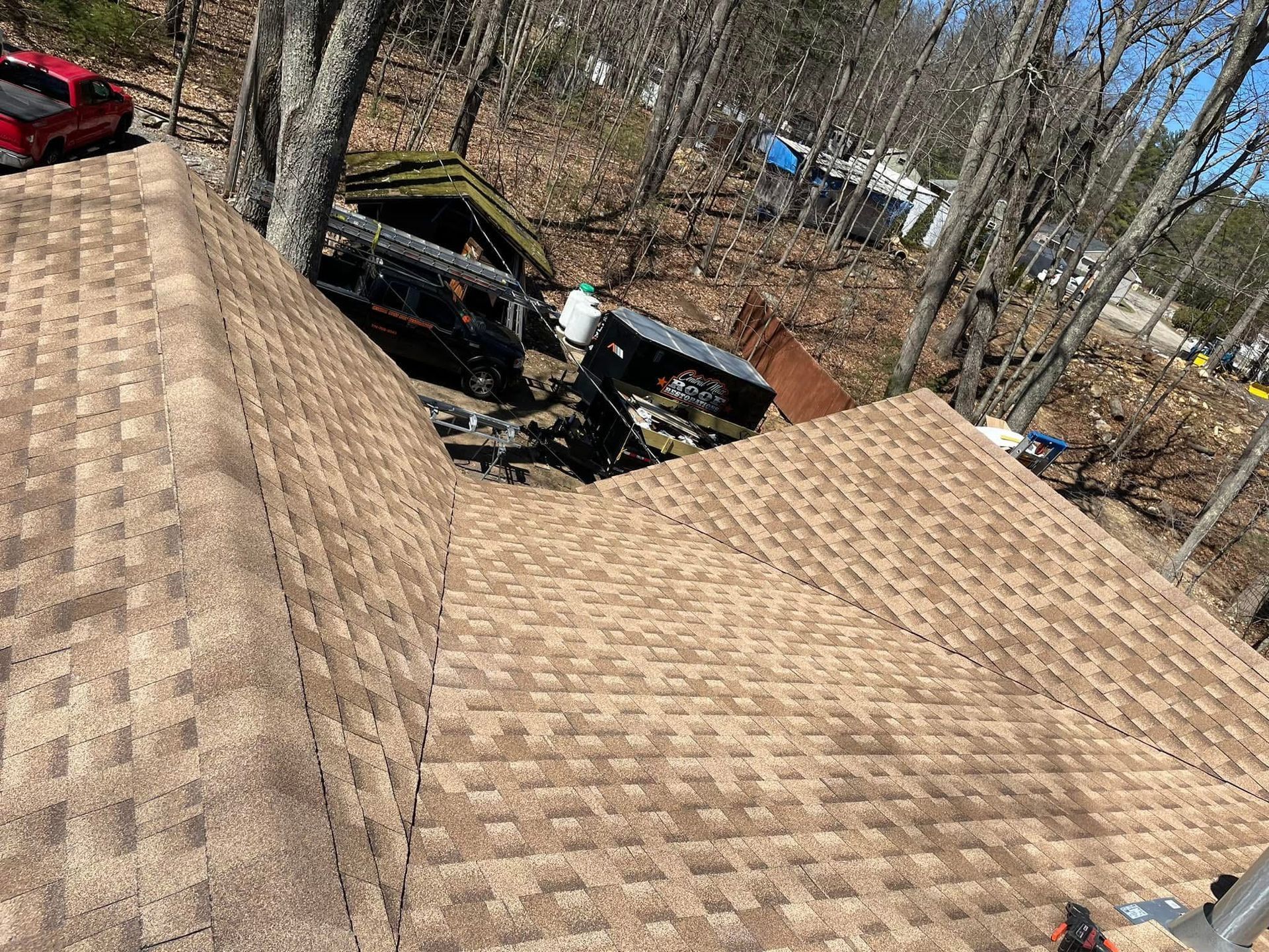 Damaged roof shingles beside a backyard pool area with a black car below trees