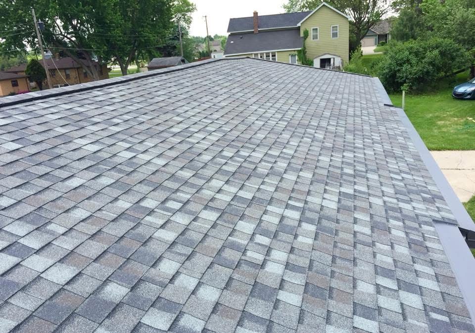 Gray shingle roof with a steep slope, viewed from above with houses and trees in the background