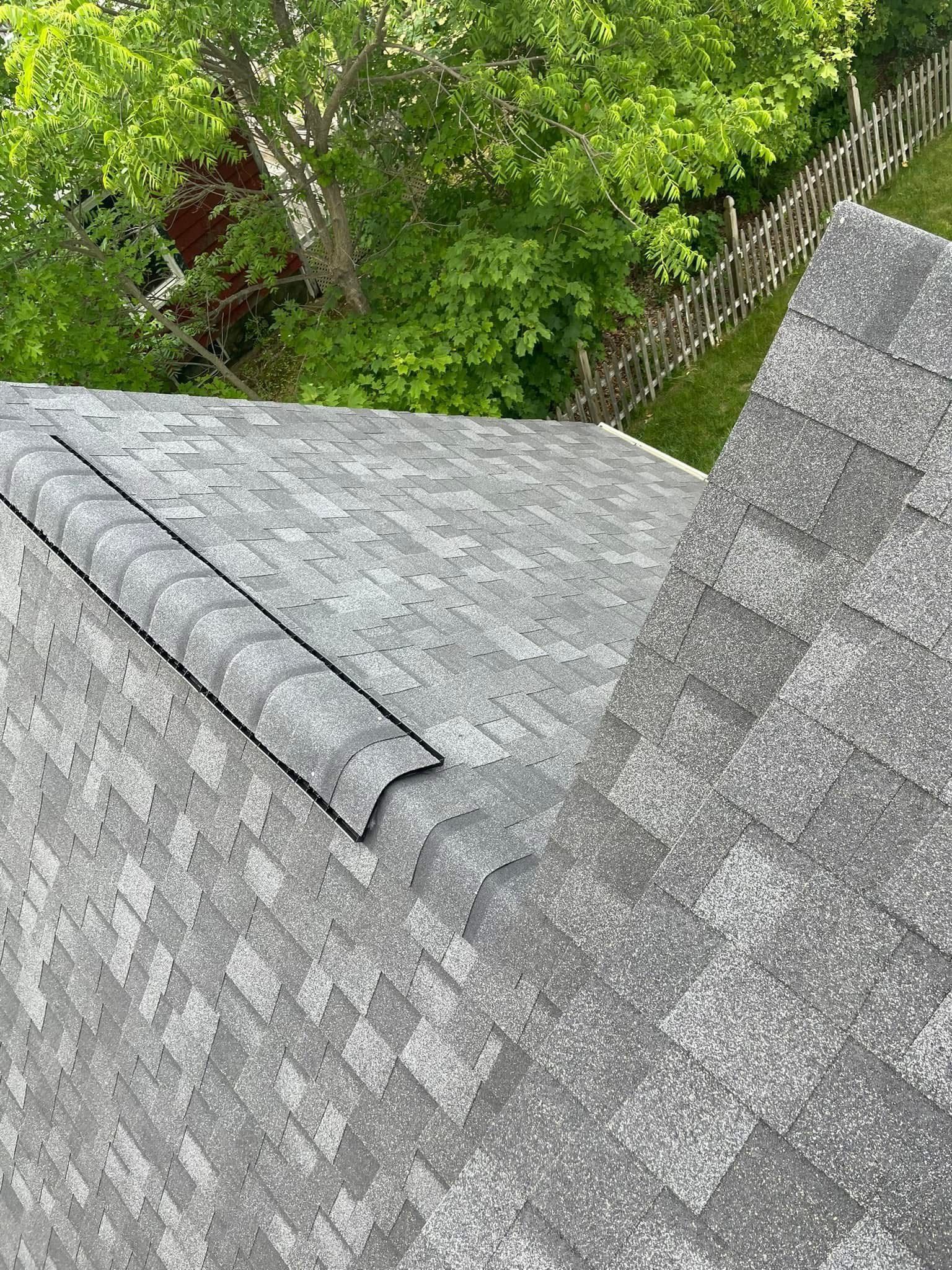 Gray shingled roof with a steep slope beside green trees and a wooden fence