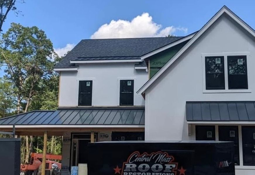 Two-story white house under construction with black roof and a roofing dumpster in front