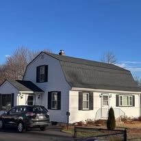 White house with dark roof and parked car under a clear blue sky