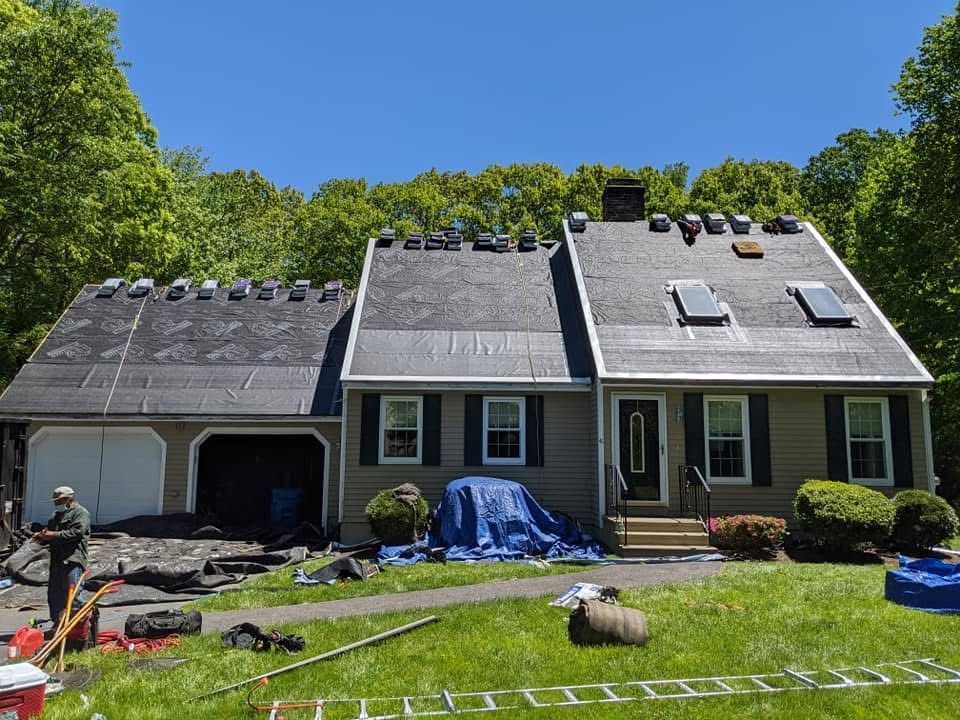 House exterior with roof under repair, ladders and tools on the lawn, and blue tarp by the front door