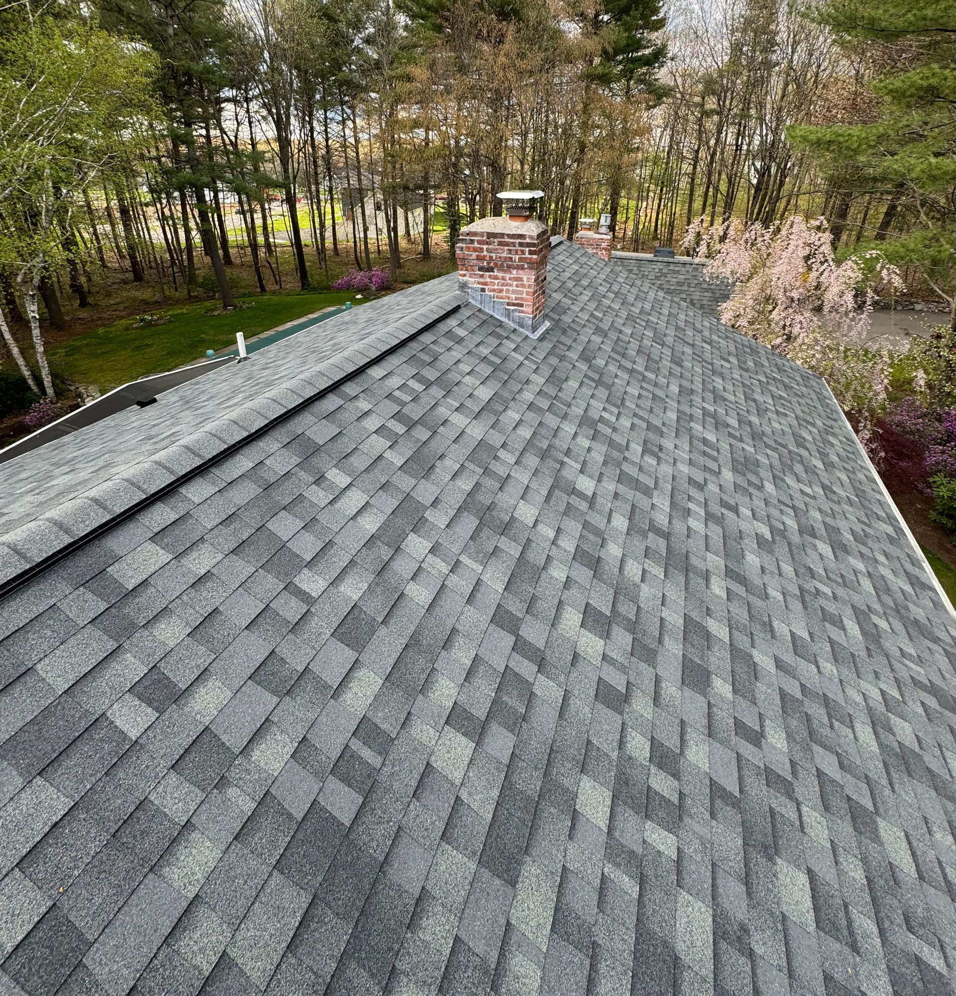 Gray shingle roof with a brick chimney, viewed from above среди trees and a wooded yard