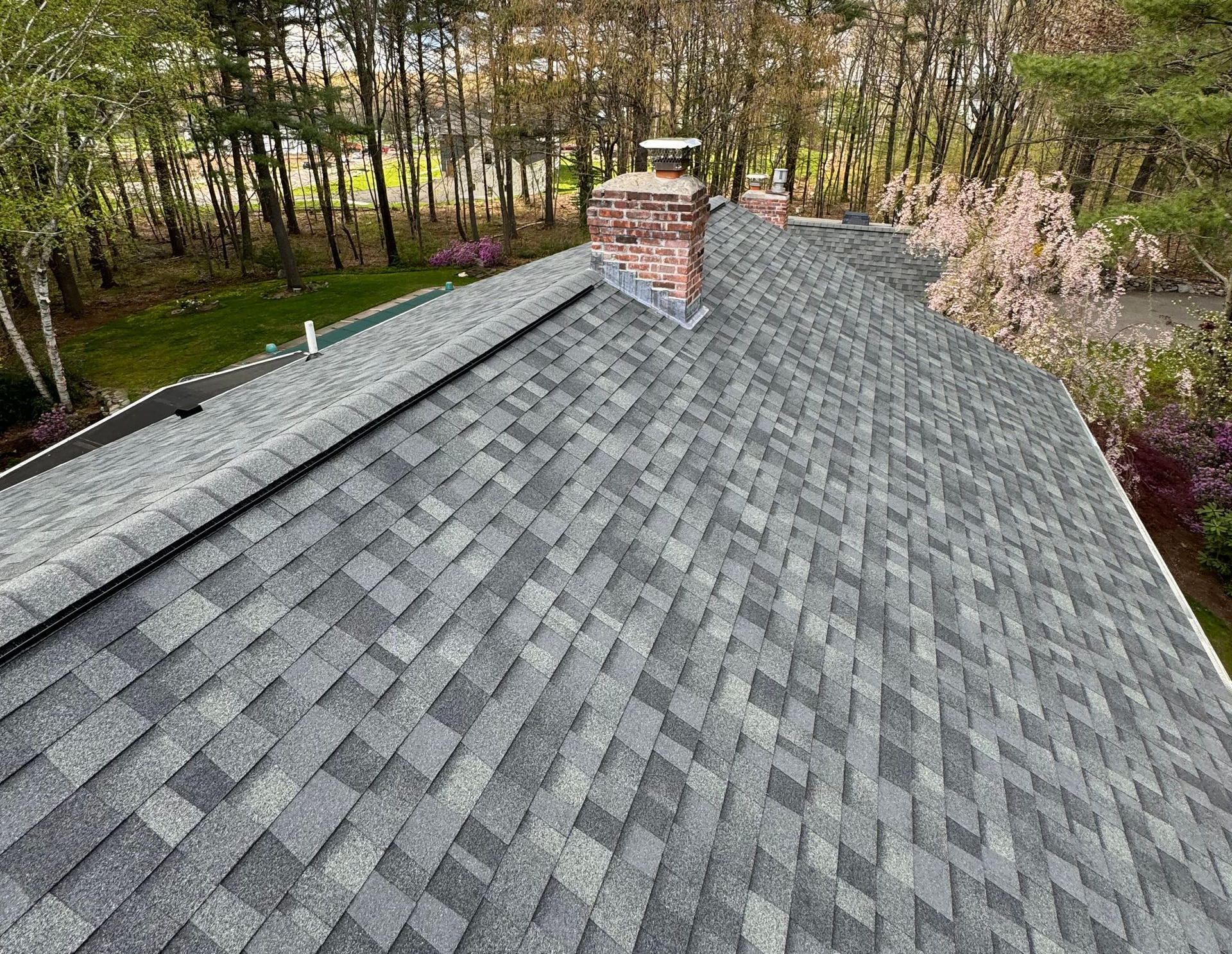 Gray shingle roof with a brick chimney, seen from above amid trees and a wooded yard.