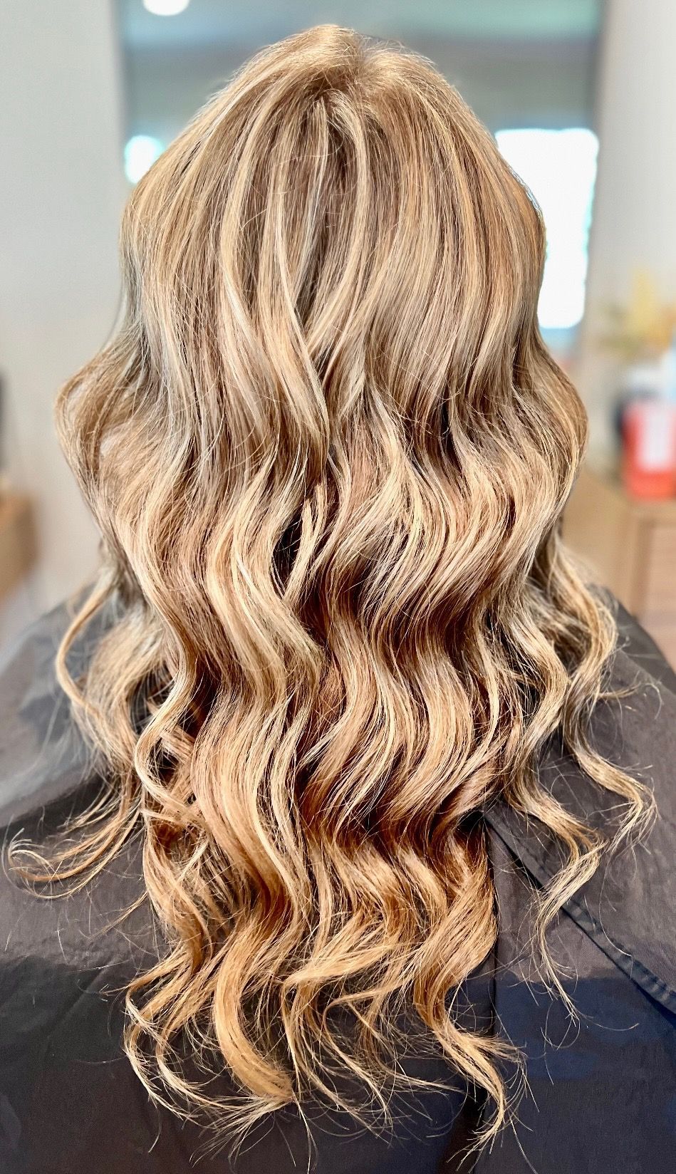Woman with long, wavy brown hair, styled in a braided crown and cascading down her back, wearing a white dress.