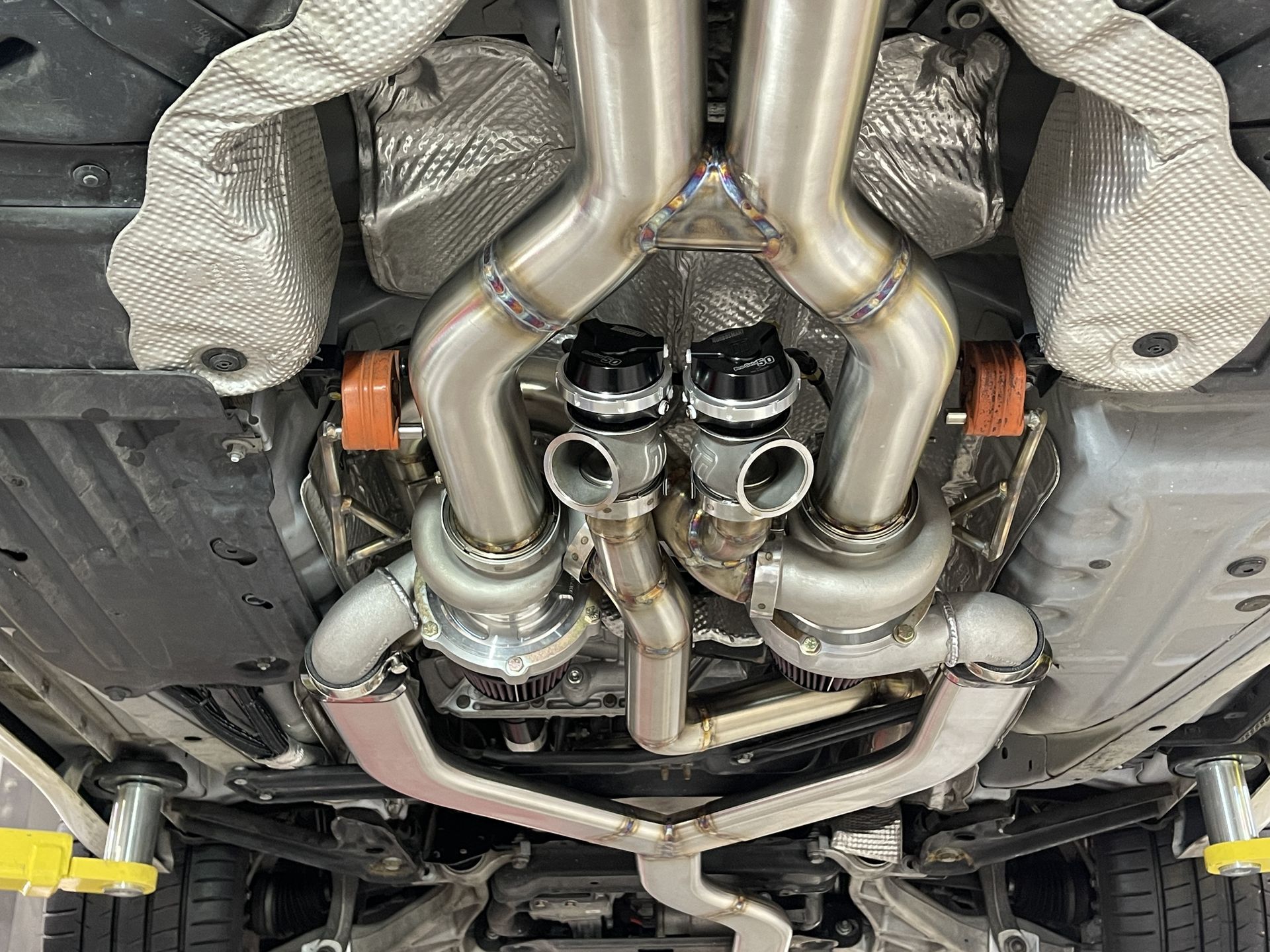 Undercarriage view of a custom exhaust system, with silver pipes, two black valves, and heat shielding.
