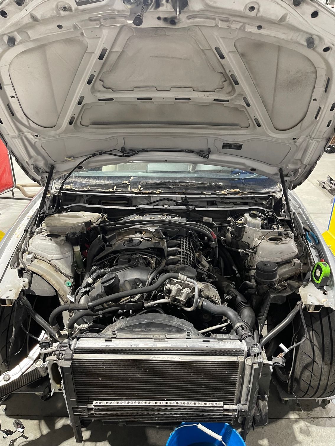 Car engine bay with hood open, radiator visible, partially disassembled for repair.