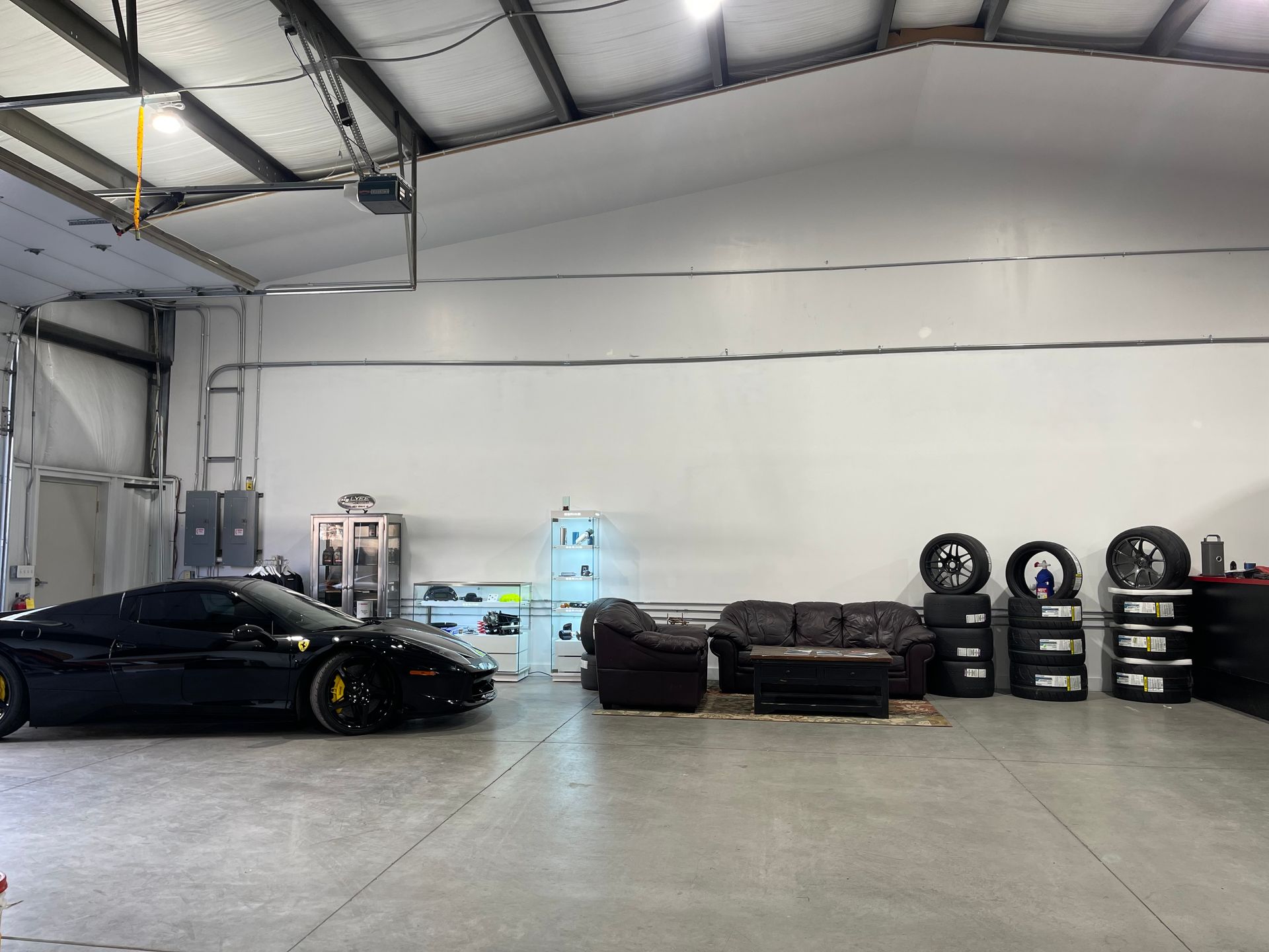 Black sports car inside a garage with seating area and stacked tires.