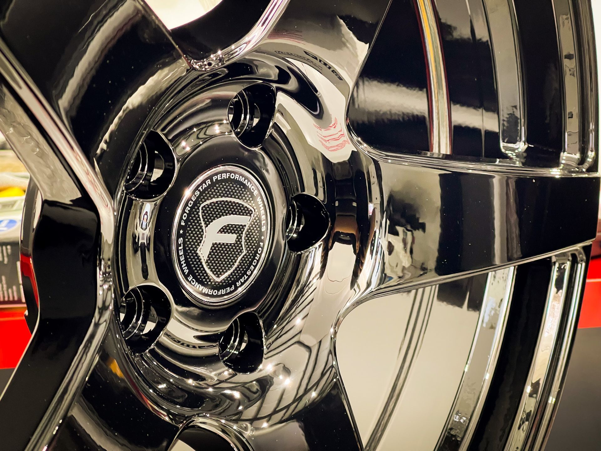 Shiny, black car rim with a logo in the center and black lug nuts.