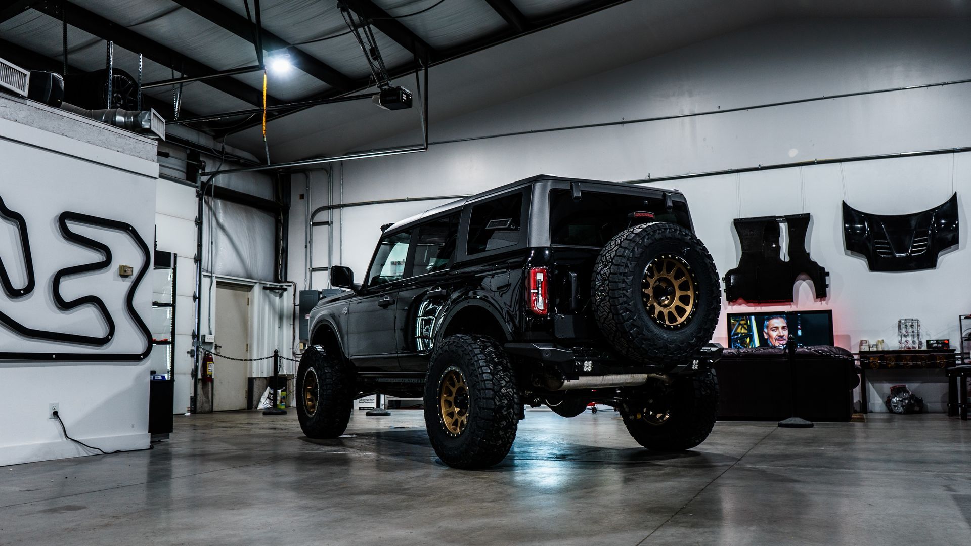 Black Ford Bronco SUV with gold wheels in a garage.