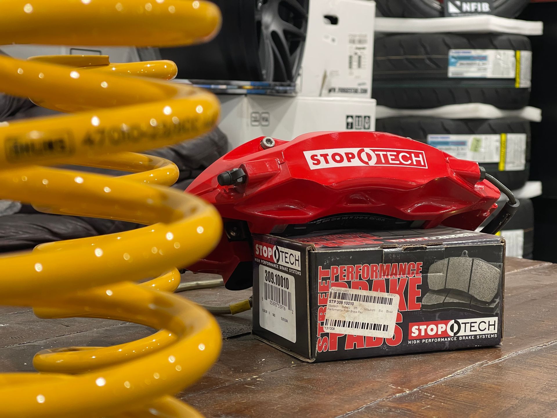 Yellow coil spring, red StopTech brake caliper, and box of StopTech brake pads on a table.