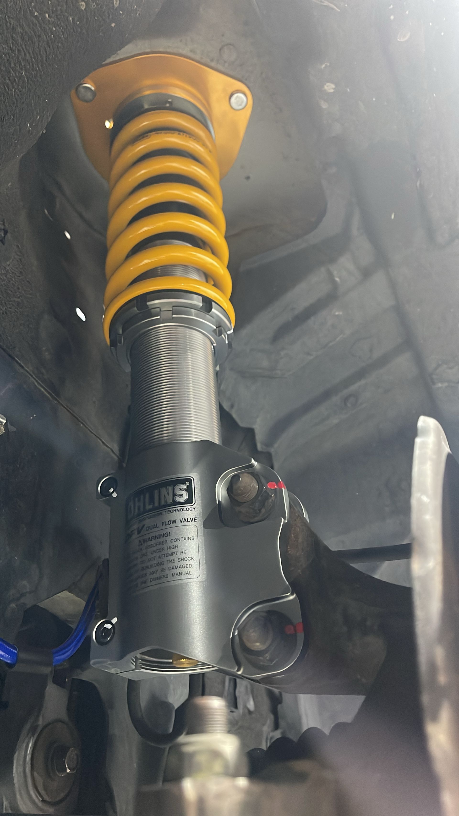Yellow coilover suspension component installed in a vehicle, with gray shock body and black bracket.