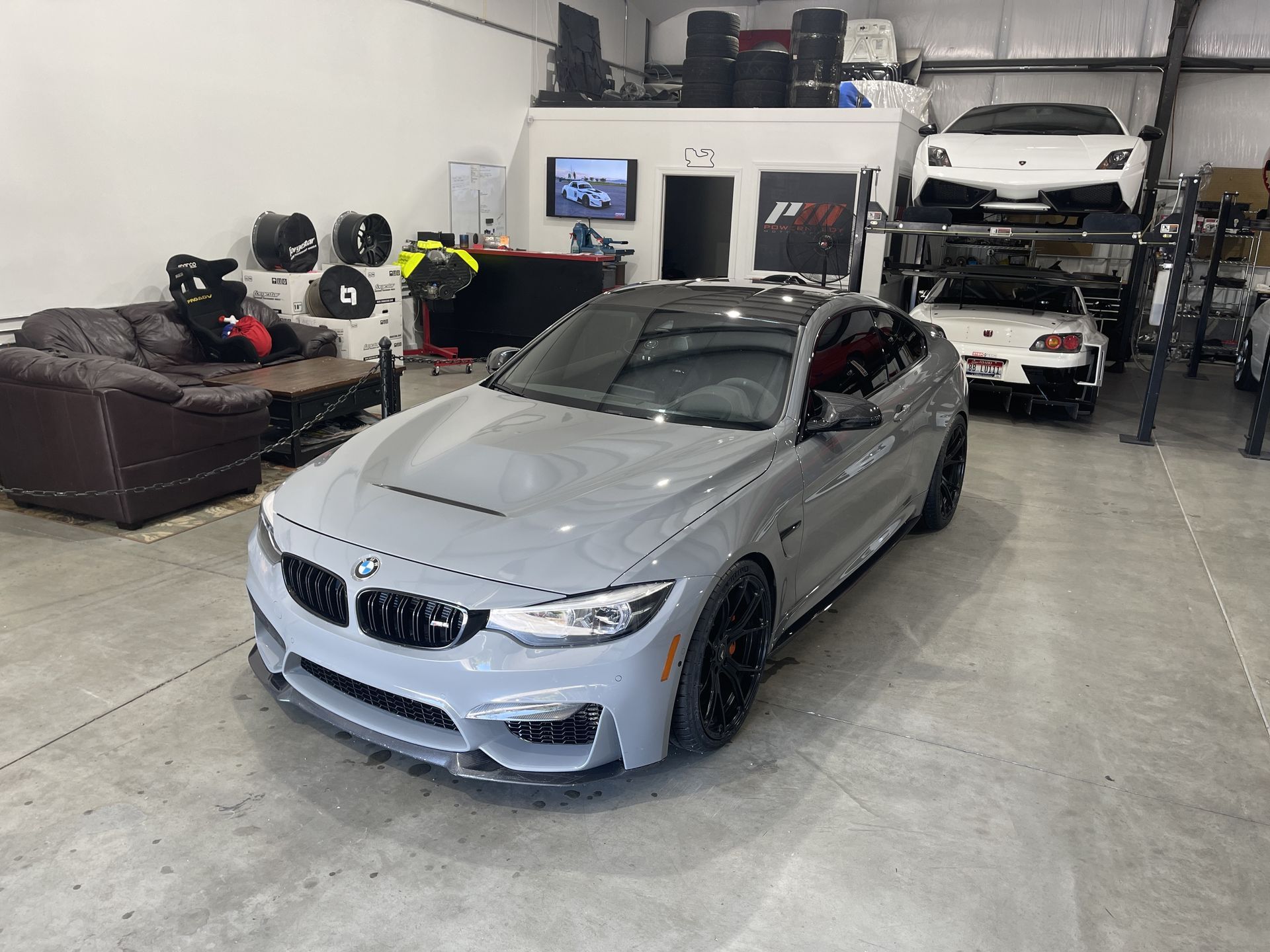 Gray BMW M4 coupe in a shop, with a sports car on a lift in the background.