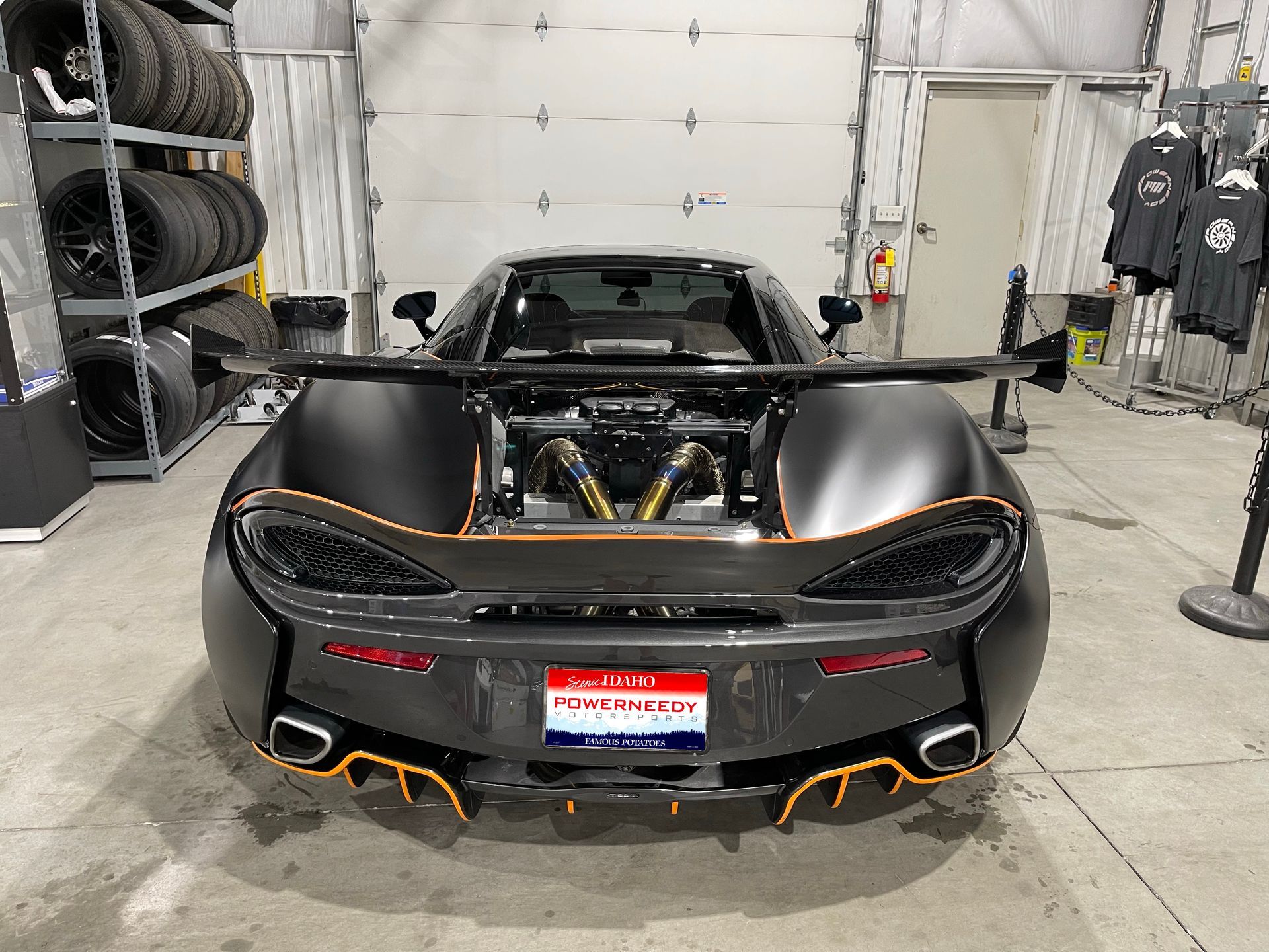 Rear view of a black McLaren sports car with orange accents, large spoiler, and modified exhaust in a garage.