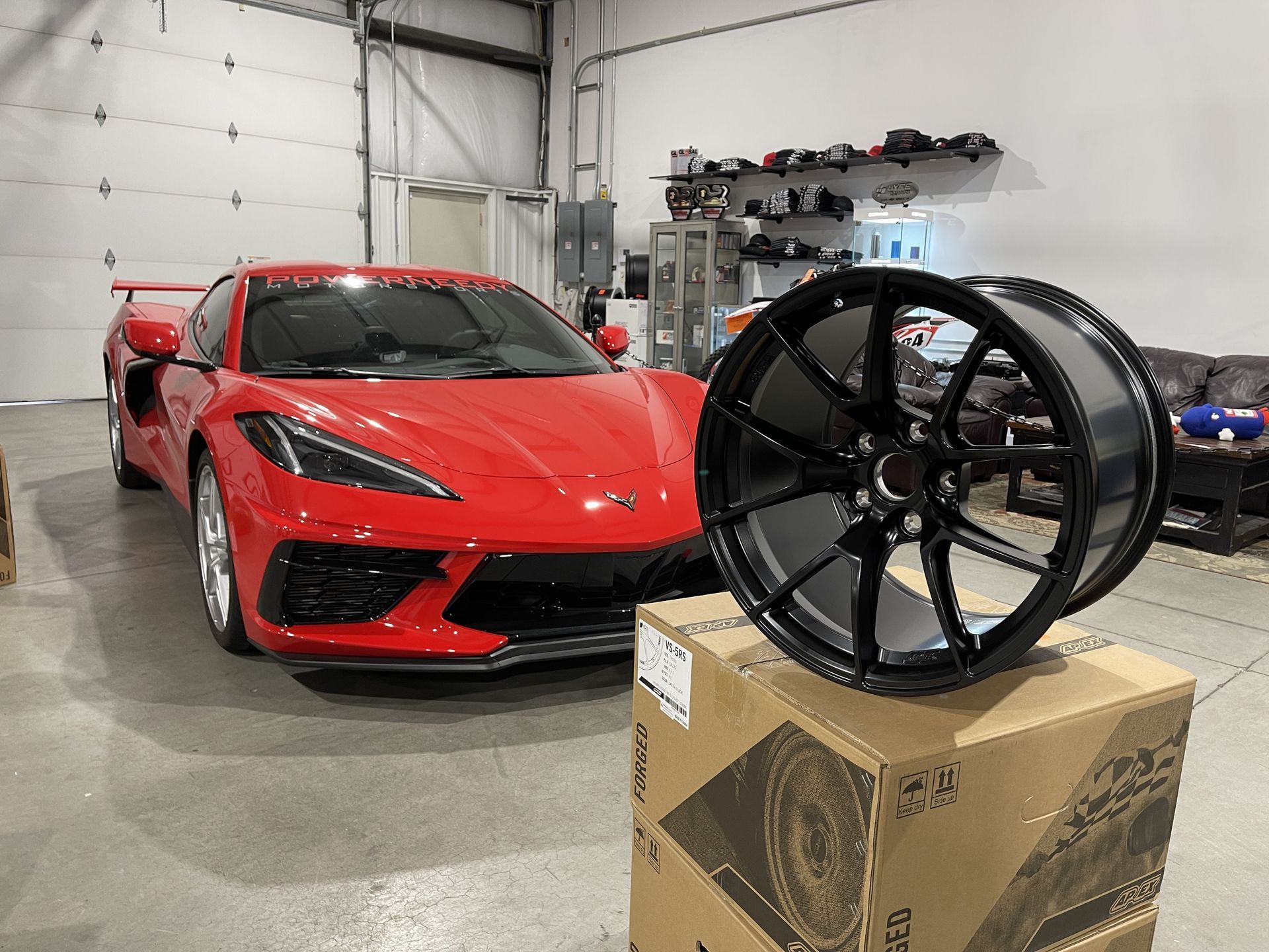 Red Corvette sports car next to a black wheel in a garage setting.