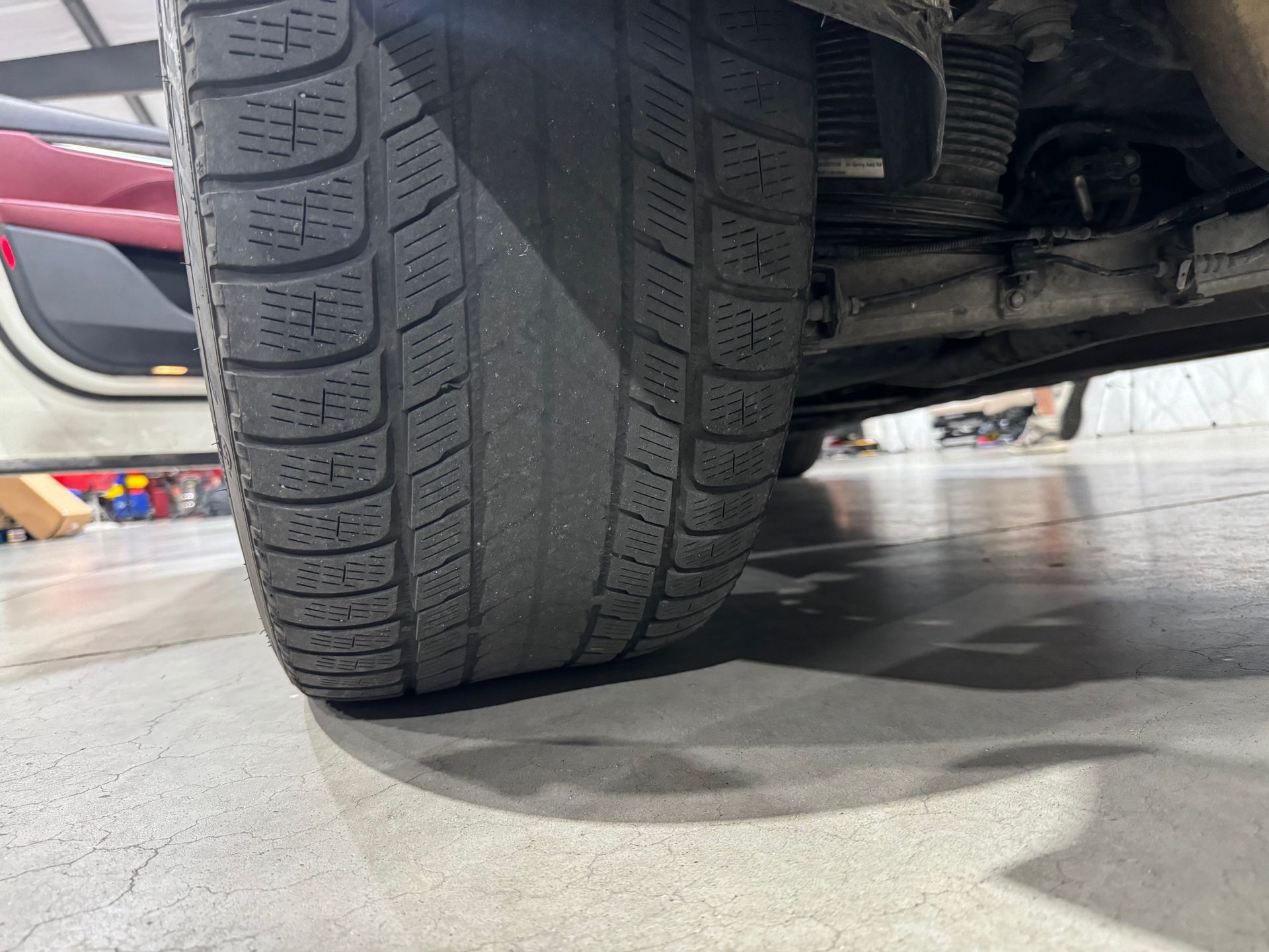 Close-up of a car tire with a textured tread, viewed from the side, on a concrete surface.