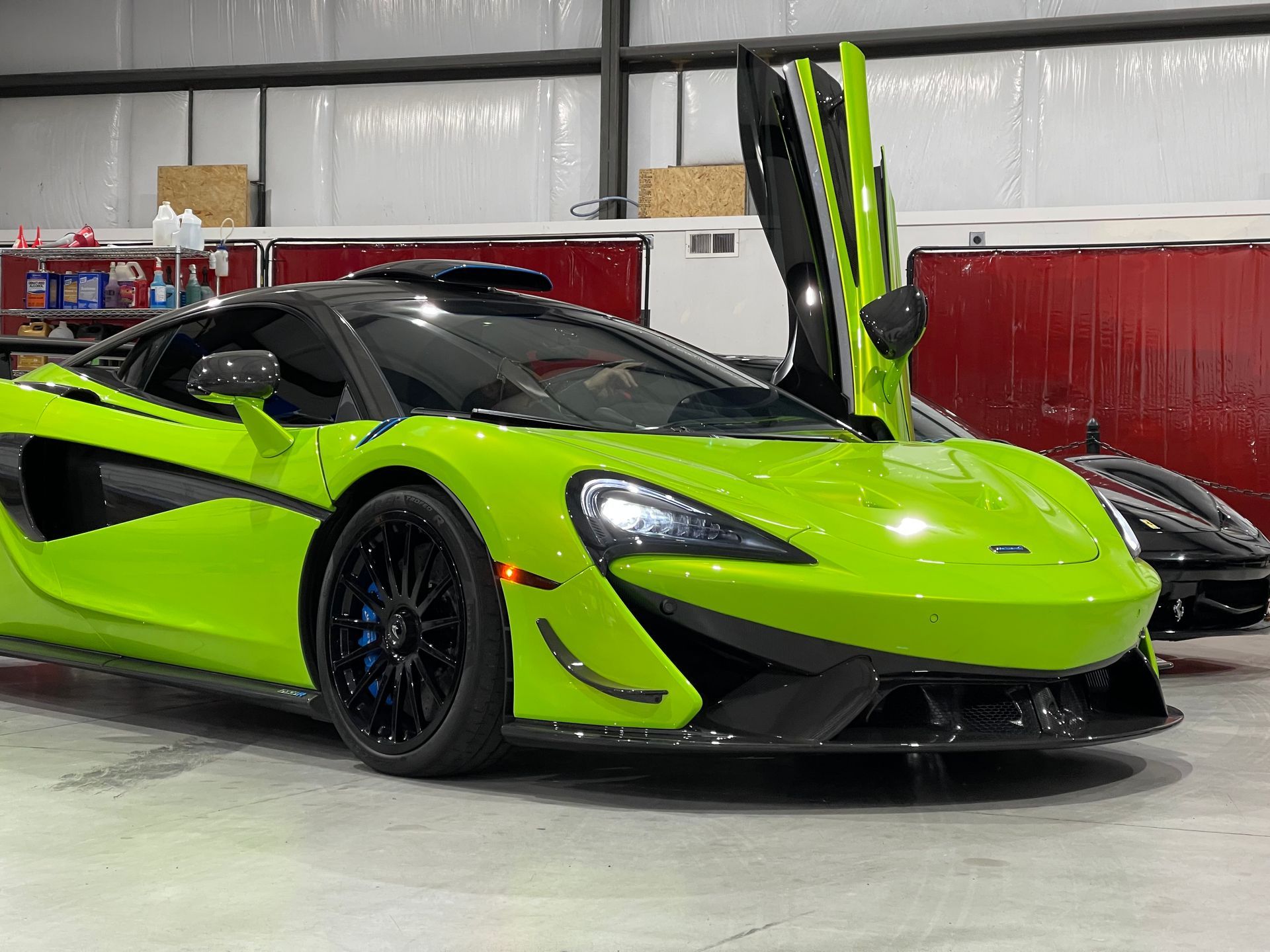 Bright green McLaren sports car with doors open in a garage.