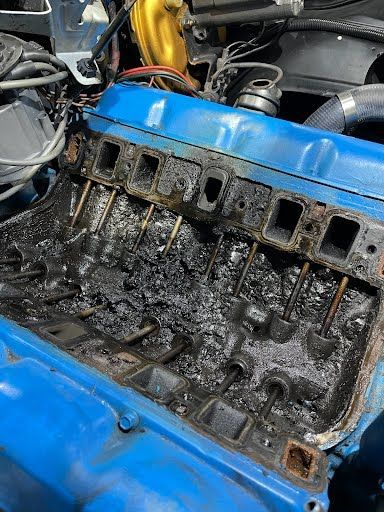 Blue engine block with exposed intake manifold ports covered in black soot and debris.