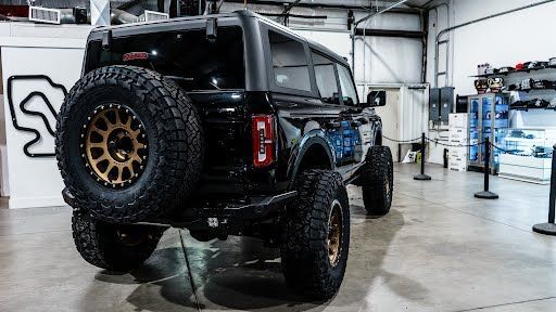 Black Ford Bronco with bronze wheels and spare tire, inside a showroom.