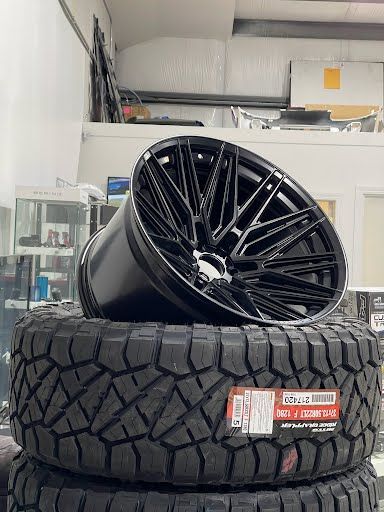Black alloy wheel resting on a stack of off-road tires, inside a shop.