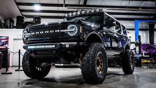 Black lifted Ford Bronco with off-road tires, gold wheels, and light bars in a garage.