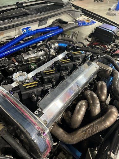 Car engine bay with blue roll cage, headers, and custom components.