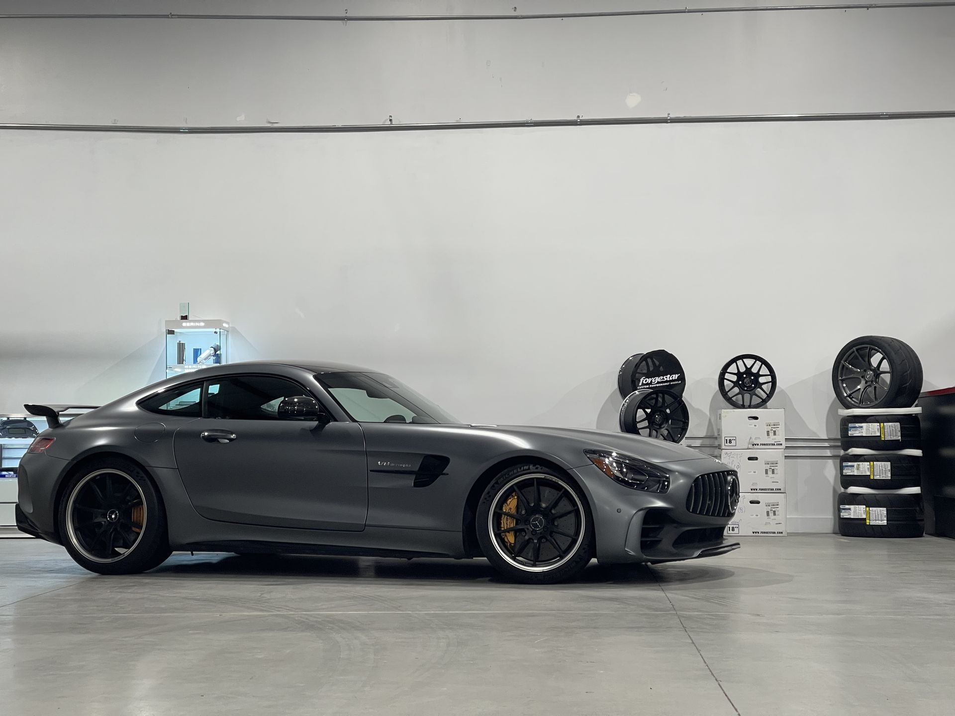Gray Mercedes-AMG GT R sports car parked in a showroom, black wheels, yellow brake calipers.