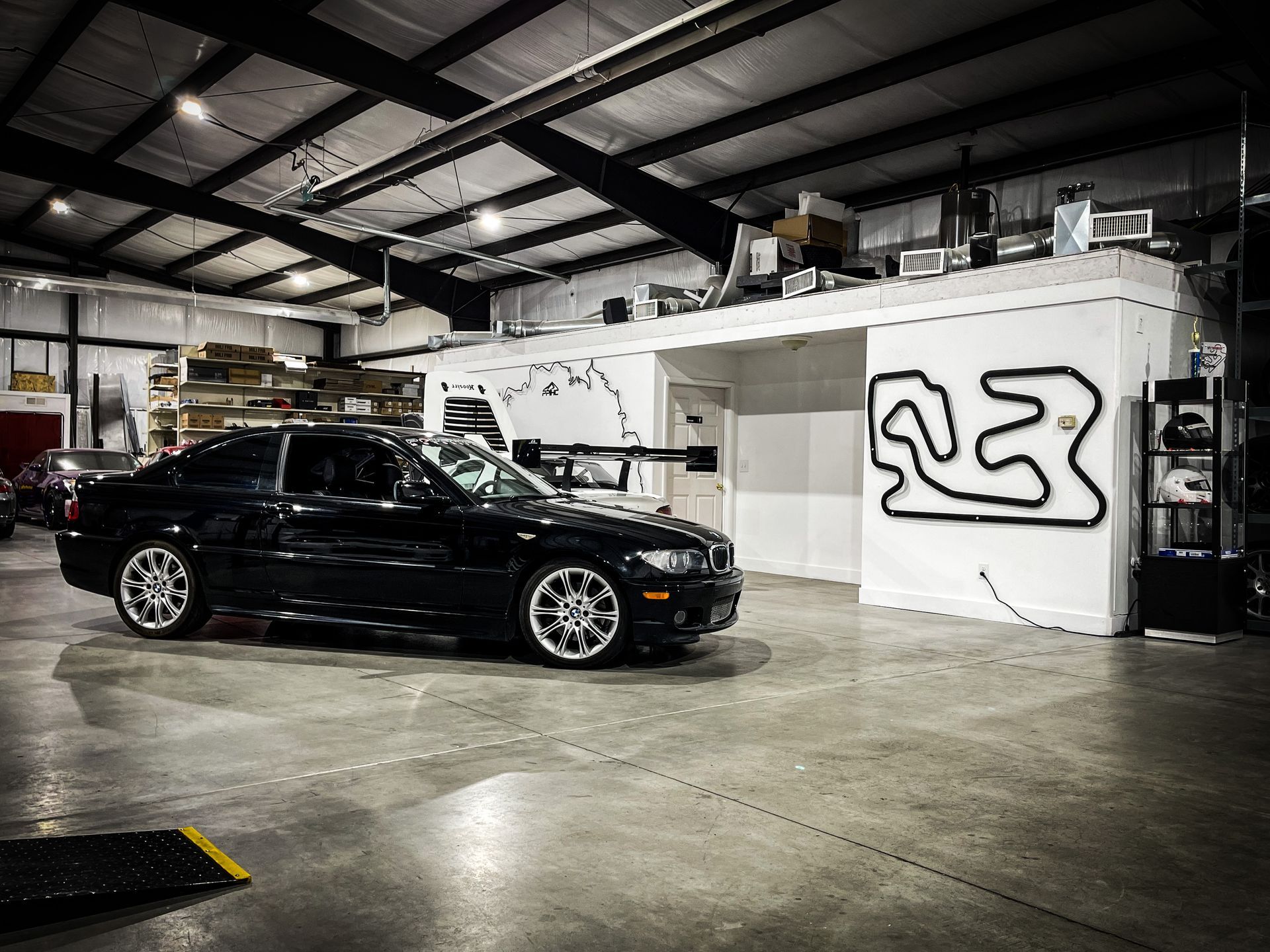 Black car inside a garage with track outline on a white wall.