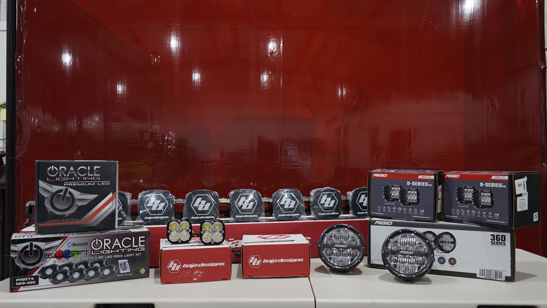 Several vehicle lights and boxes on a white surface in front of a red backdrop.