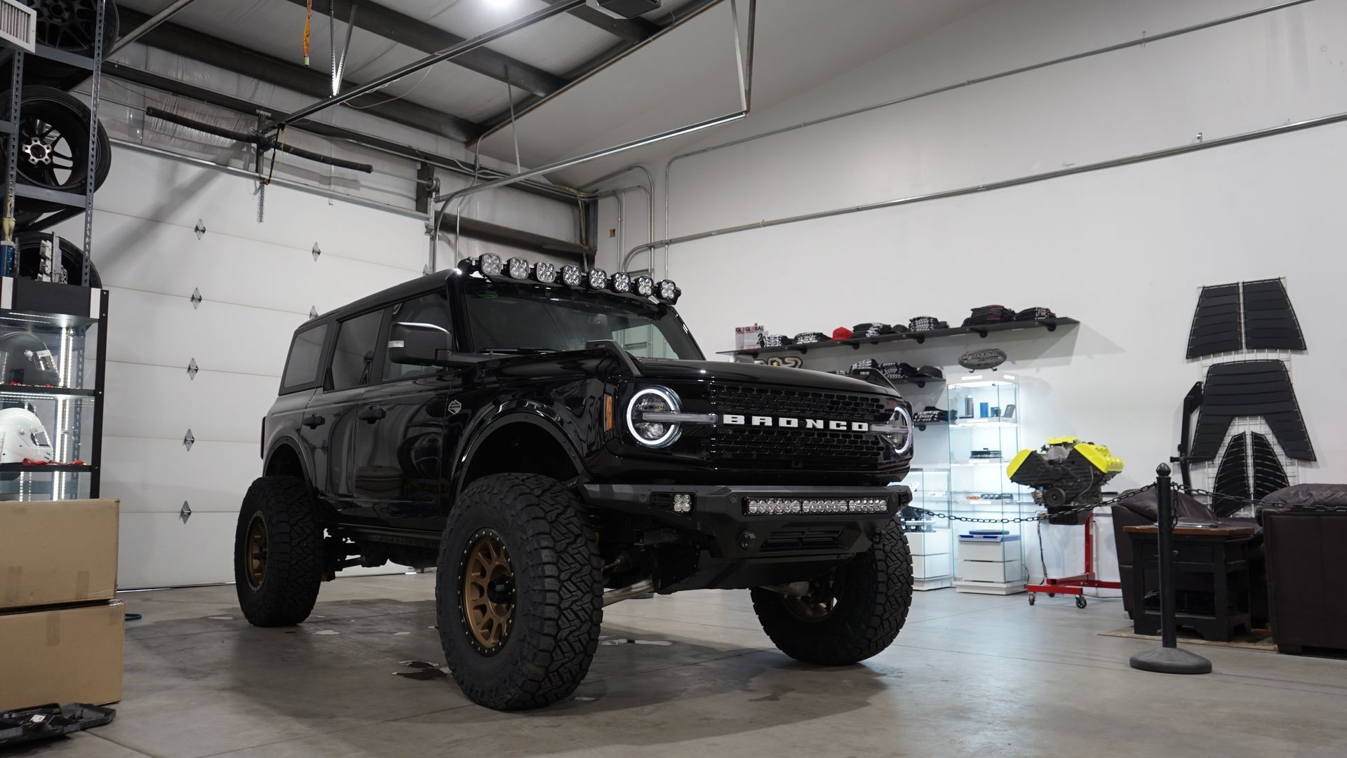 Black off-road Ford Bronco in a garage. It has large tires, roof lights, and a custom front bumper.