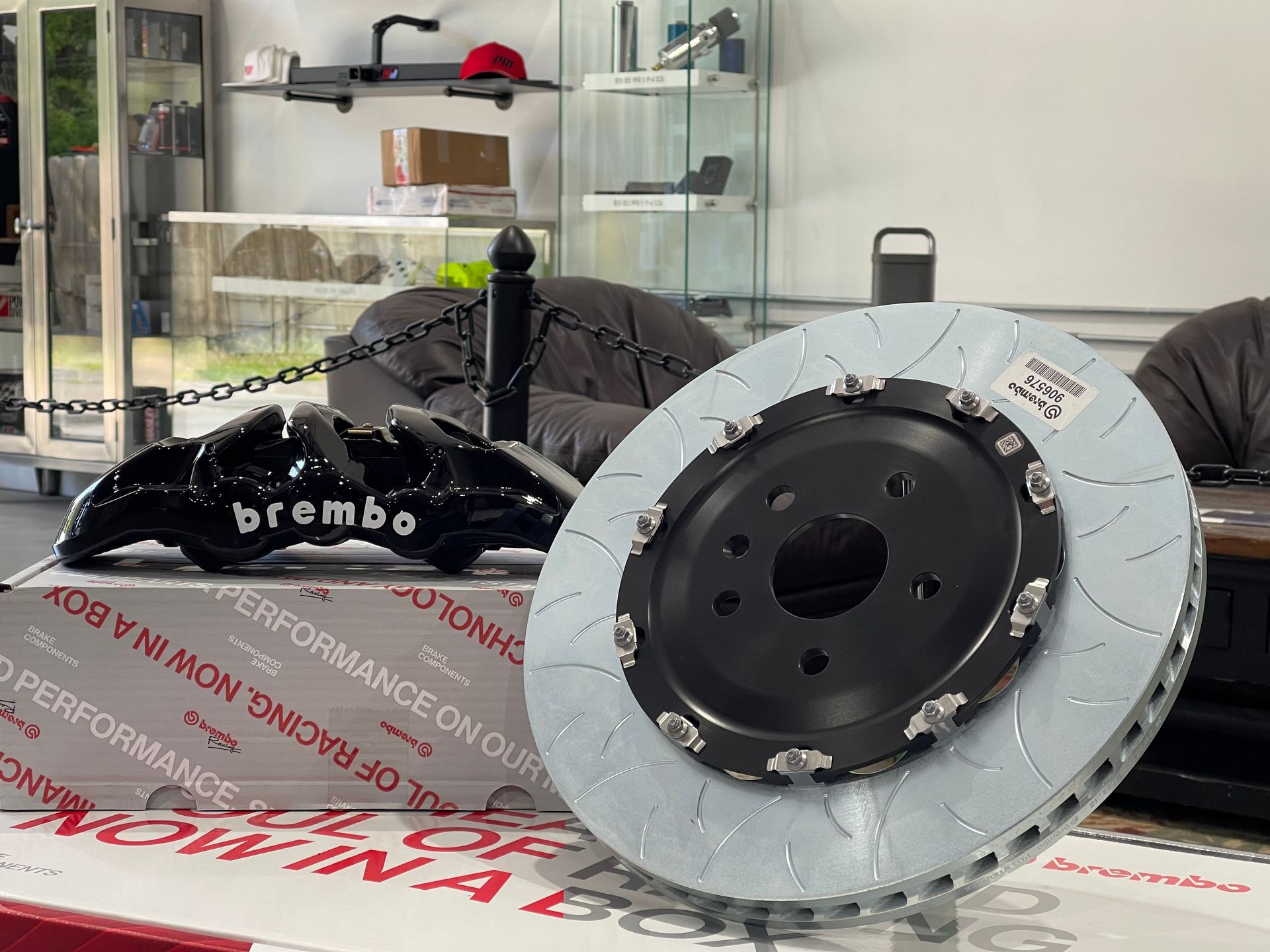 Brembo performance brake kit: black caliper next to a slotted brake rotor. White box in the foreground.