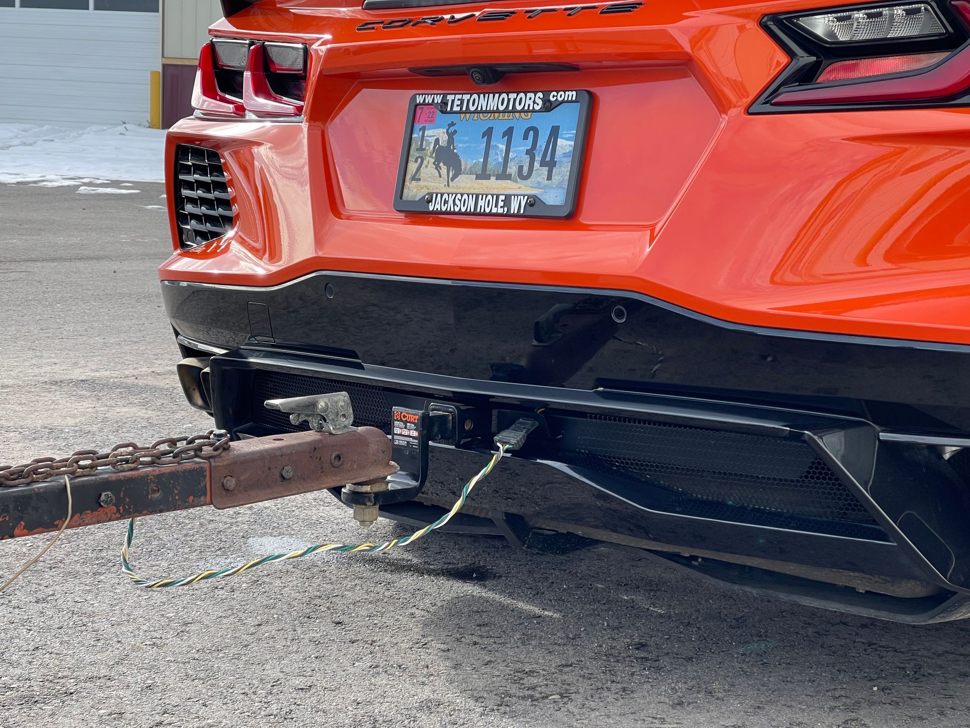 Orange Corvette with a trailer hitch connected to a rusty trailer.
