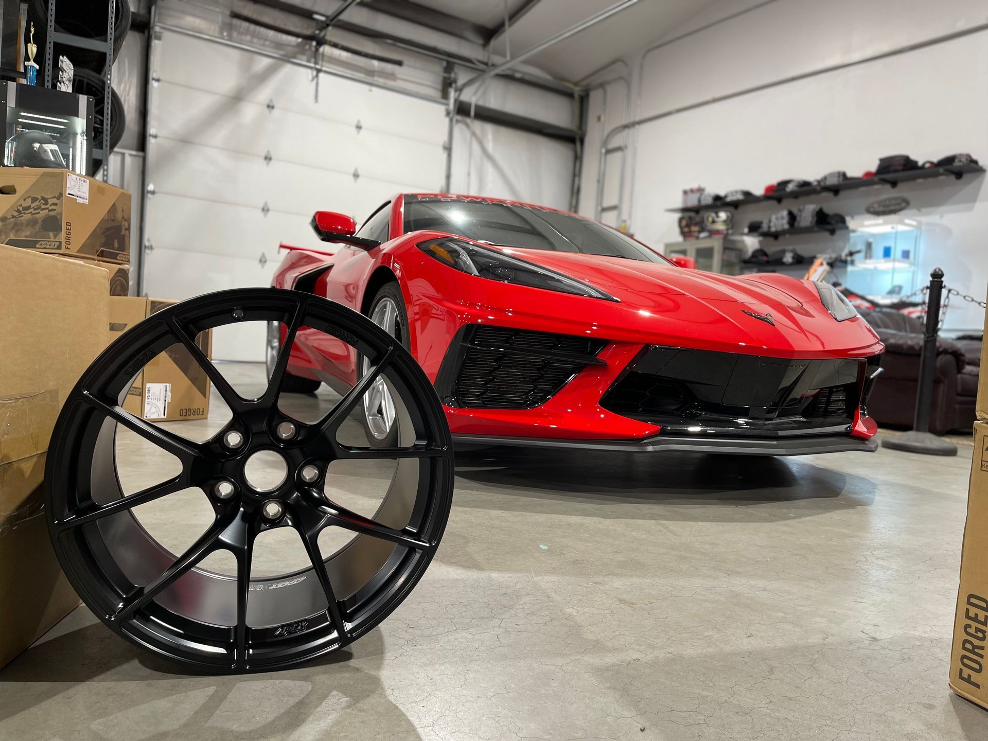 Black wheel in front of a red sports car inside a garage.