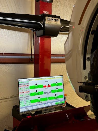 A white car tire aligned on a Hunter alignment machine, display showing readings in green and red.