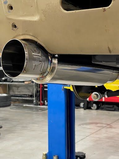Shiny chrome exhaust pipe, angled and welded, attached to a car's underside, in a garage setting.