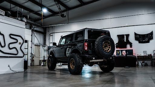 Black Ford Bronco SUV with gold wheels in a garage.