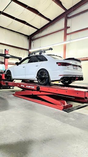 White car on a red lift in a garage. Black wheels and roof rack visible.