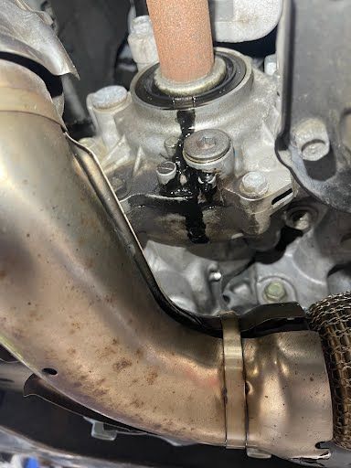 Engine component leaking dark fluid. Exhaust pipe visible.