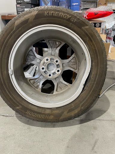 Bent silver alloy wheel with mounted tire, likely damaged from impact.