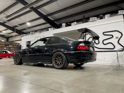 Black BMW coupe with bronze wheels and a large wing parked indoors.