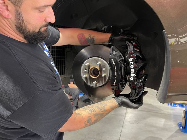 Mechanic installing a black Brembo brake caliper on a car, inside a workshop.
