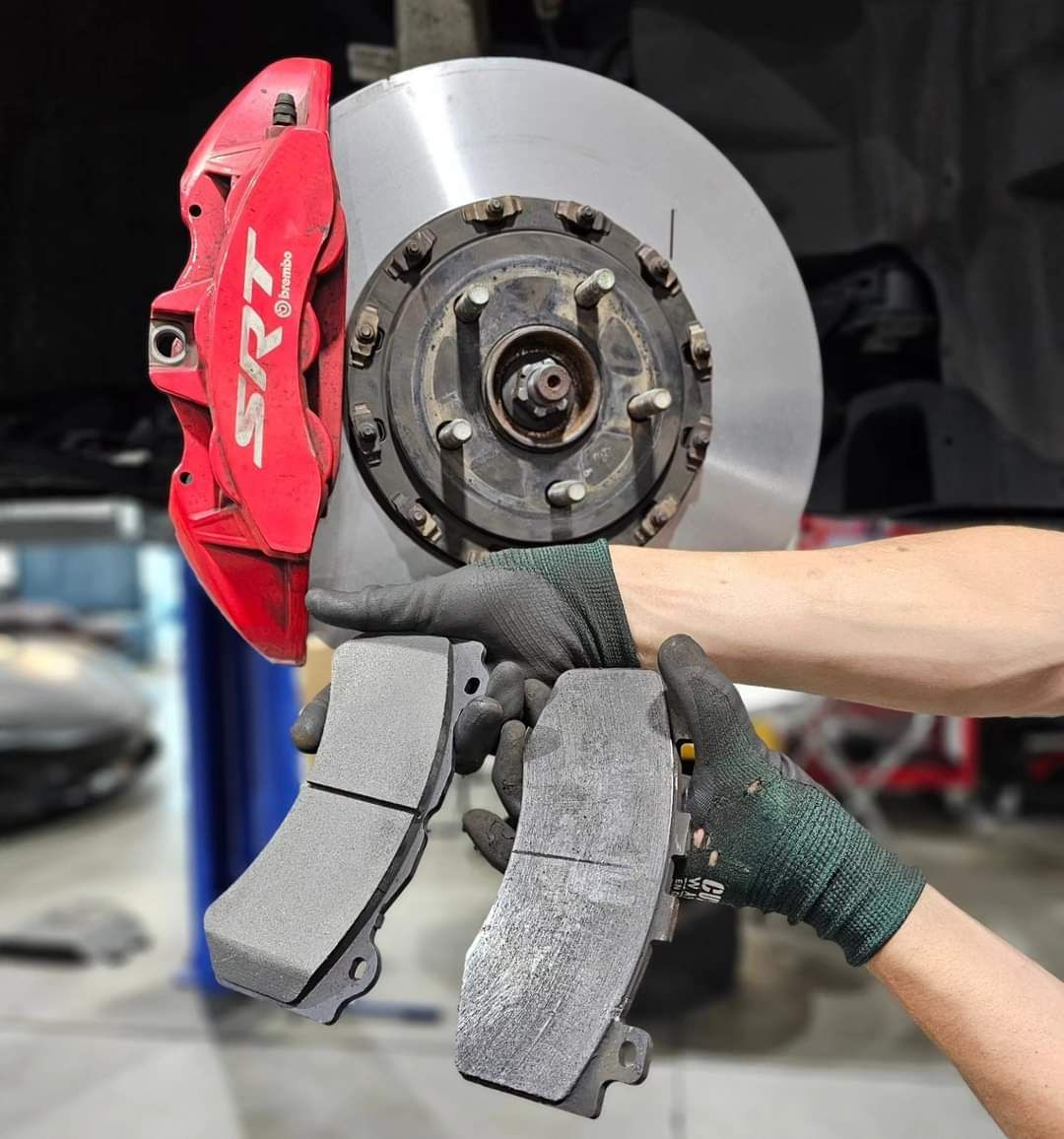 Person holding brake pads next to a red SRT caliper and rotor in a garage.